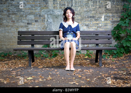 Japanische Mädchen sitzen auf Holzbank mit Wecker Stockfoto