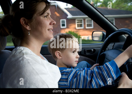 Ein kleiner Junge sitzt auf seiner Mutter s Runde und behauptet, dass er das Fahrzeug fährt Stockfoto