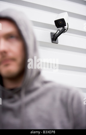 Überwachungskamera und junger Mann In Sweatshirt mit Kapuze Stockfoto