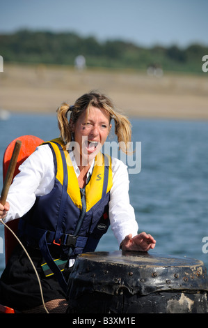 Drachenbootrennen auf Bewl Wasserbehälter Schlagzeuger wie ein St Trinian gekleidet schreit ihr paddeln-Team. Stockfoto