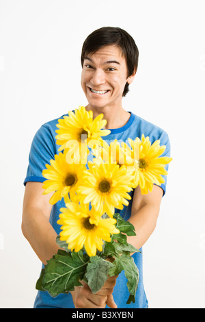 Asiatische junge Mann hält Bouquet von gelben Gerber Gänseblümchen lächelnd Stockfoto