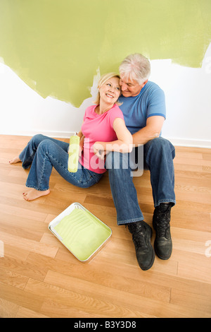 Porträt von Erwachsenen Brautpaar sitzt vor halb gemalt Wand mit Farbe versorgt kuscheln Stockfoto