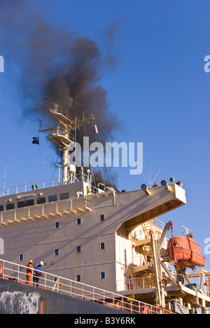 Schwarzer Rauch steigt vom Schiff des Trichters nähert sich das Schiff am Kai. Stockfoto