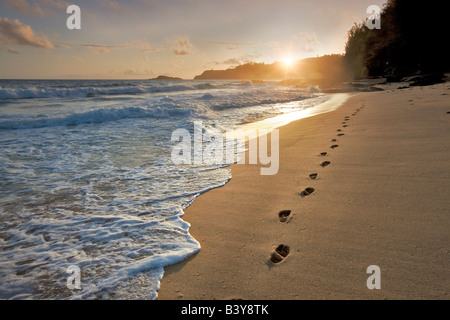 Sonnenaufgang am Secret Beach mit Fußspuren im Sand Kauai Hawaii Stockfoto