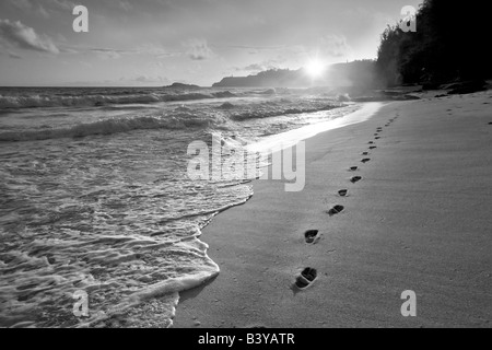 Sonnenaufgang am Secret Beach mit Fußspuren im Sand Kauai Hawaii Stockfoto