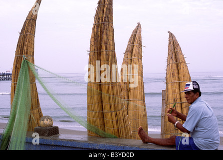 Peru, La Libertad, Huanchaco. Ein Pescador (Fischer) flickt sein Netz vor einer Reihe von Totora (Schilf) Booten. Die Boote genannt Caballitos de Totora (Pferdchen Schilf) wurden verwendet von den lokalen Fischern seit über zweitausend Jahren verwendet. Stockfoto