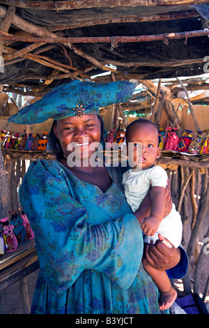 Namibia, Damaraland, Twyfelfontein. Eine Herero-Frau in traditioneller Kleidung hält ihr Baby am Straßenrand stand im Damaraland. Stockfoto