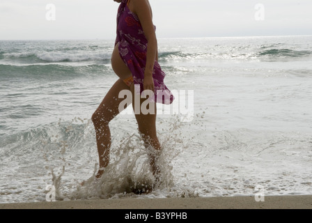 Eine Schwangere, die am Strand entlang läuft und Wasser spritzt, trägt eine Bluse über einem Badekostüm. Canet Plage bei Perpignan Südfrankreich 2008 Stockfoto