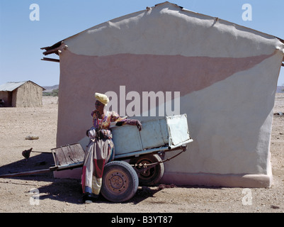 Namibia, Damaraland, Palmwag. Eine Herero-Frau ruht neben einem Eselskarren vor ihrem attraktiv bemalten Haus. Die aufwendige dr Stockfoto