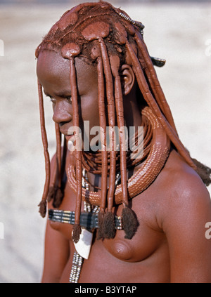 Namibia, Kaokoland, Empembe. Ein Himba-Mädchen in traditioneller Kleidung. Ihr Körper glänzt aus einer Mischung von rotem Ocker, Butterfett und Kräutern. Ihr langes Haar ist in der traditionellen Himba Weise gestaltet. Ihr große, Runde weiße Perlen Halskette, genannt Ombwari, wird von beiden Geschlechtern getragen. Die Himba sind Bantu Herero sprechende Nomaden, die in der rauen, trockenen aber krass schöne Landschaft entlegenen Nordwesten Namibias Leben. Stockfoto