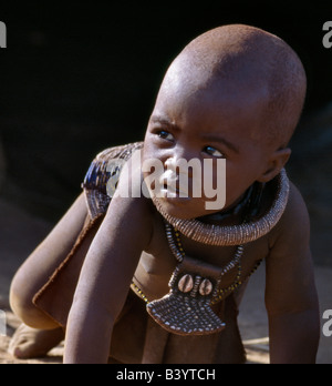 Namibia, Kaokoland, Epupa. Ein kleiner Junge, seinen Körper verschmiert mit einer Mischung aus rotem Ocker, Butterfett und Kräuter, trägt eine Runde weiße Perlen Halskette, genannt Ombwari, eine Tradition der Himba ausgerechnet. Seine anderen Ornament besteht aus Metallperlen gesichert auf Leder und ist verziert mit zwei Kauris von Afrikas Atlantic Coastline.The Himba sind Bantu Herero sprechende Nomaden, die in das harte Leben, trocken aber sehr schöne Landschaft entlegenen Nordwesten Namibias. Stockfoto