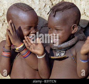Namibia, Kaokoland, Epupa. Zwei glückliche Himba-Mädchen mit ansprechenden Frisuren klatscht im Takt eines Tanzes. Ihren Schmuck gehören weiße Perlen Halsketten, genannt Ombwari, eine Tradition der Himba ausgerechnet. Einer von ihnen trägt auch eine Dekoration Metallperlen gesichert auf Leder, verziert mit zwei Kauris von Afrikas Atlantic Coastline.The Himba sind Bantu Herero sprechende Nomaden, die in der rauen, trockenen aber krass schöne Landschaft entlegenen Nordwesten Namibias Leben. Stockfoto