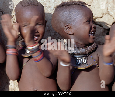 Namibia, Kaokoland, Epupa. Zwei glückliche Himba-Mädchen mit ansprechenden Frisuren klatscht im Takt eines Tanzes. Ihren Schmuck gehören weiße Perlen Halsketten, genannt Ombwari, eine Tradition der Himba ausgerechnet. Sie tragen auch Metallperlen gesichert auf Leder, verziert mit Kaurimuscheln aus Afrikas Atlantic Coastline.The Himba sind Bantu Herero sprechende Nomaden, die in das harte Leben, trocken aber sehr schöne Landschaft entlegenen Nordwesten Namibias. Stockfoto