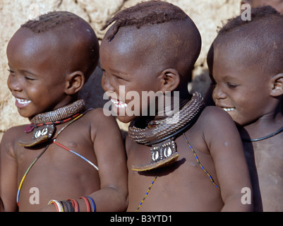 Namibia, Kaokoland, Epupa. Drei glückliche Himba-Kinder - zwei Mädchen und ein Junge - viel Spaß beim Betrachten eines Tanzes. Die Mädchen Verzierungen gehören weiße Perlen Halsketten, genannt Ombwari, eine Tradition von allen Himba Leute und Metallperlen gesichert auf Leder, das mit Kauris von Afrikas Atlantic Coastline.The Himba verziert sind Bantu Herero sprechende Nomaden sind, die in der rauen, Leben aber sehr schöne Landschaft entlegenen Nordwesten Namibias trocknen. Stockfoto