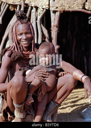 Namibia, Kaokoland, Epupa. Ein Himba Mutter und Baby Sohn außerhalb ihres Heimatlandes kuppelförmigen entspannen.  Ihre Körper glänzen aus einer Mischung Stockfoto