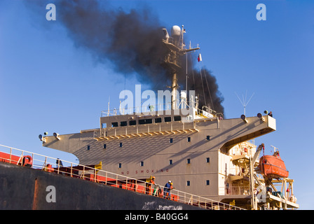 Schwarzer Rauch steigt vom Schiff des Trichters nähert sich das Schiff am Kai. Stockfoto