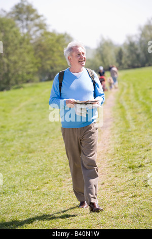 Mann, die Wanderkarte im Freien halten lächelnd mit Menschen im Hintergrund Stockfoto