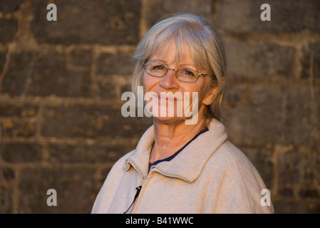 Eine Frau in ihrem 50er Jahre, mit einer Steinmauer Hintergrund in frühen Herbstsonne. Stockfoto