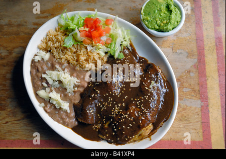 Chicken Enchiladas mit einer Mole Poblano Sauce und Reis und Bohnen mit Käse und eine Beilage der Guacamole. Stockfoto