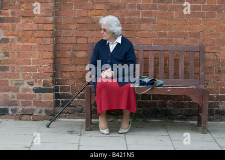 Ältere Frau sitzt alleine auf einer Holzbank UK Stockfoto
