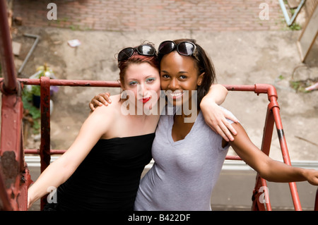 Zwei junge Frauen weiß und schwarz stehen mit einem Arm um den anderen Wange an Wange auf eine Feuerleiter, die auf der Suche nach oben Stockfoto