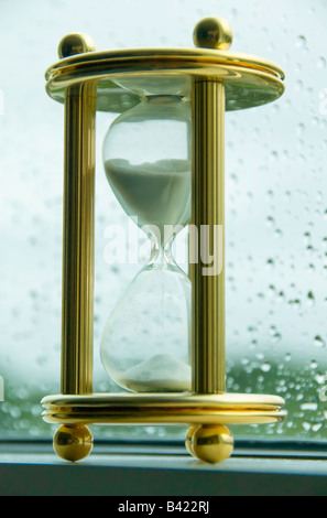 Sanduhr auf gold Stand auf Sims durch Regen bespritzt Fenster Stockfoto