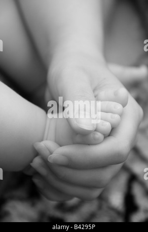 Nahaufnahme einer Mutter mit ihrem Baby Fuß in der Hand, monochromes Bild. Stockfoto