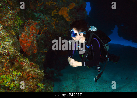 Eine einzelne weibliche Taucher massive Korallenriff Formationen mit Höhlen und schwimmen durch Tunnel zu erkunden. Stockfoto