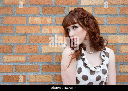 Nahaufnahme von eine junge rothaarige Frau im gepunkteten Kleid vor einer Mauer steht. Stockfoto