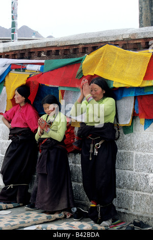 Drei Frauen beten, mit Gebetsfahnen dahinter vor Jokhang-Tempel in Barkhor Square, Lhasa, Tibet, Asien Stockfoto