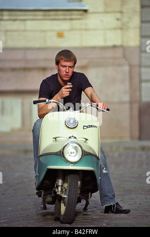 Junger Mann mit einem Mobiltelefon auf einem Motorrad, Riga, Lettland Stockfoto