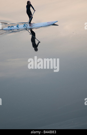 junge Teenager-Mädchen Frau tragen Neoprenanzug paddeln aufstehen Surfbrett flach ruhigen Wasser spiegeln Stockfoto