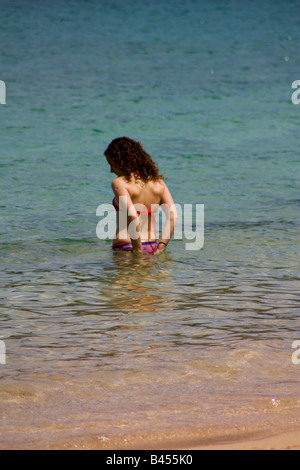 Panama, Isla Grande, junge Frau geht in die kristallklaren Wasser der Karibik, während sie ihrem Bikini behebt Stockfoto