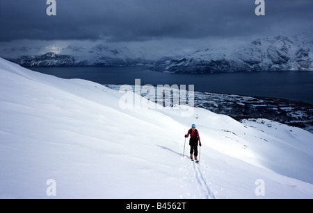 Skifahrer erklimmen eines Berges bei Sonnenschein mit Gewitterwolken über ferne Fjord und die Berge, Lyngen Alpen, arktische Norwegen hereinkommen Stockfoto