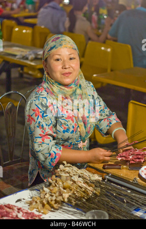 Muslimische Frau machen Schaschlik auf dem Nachtmarkt in Jiayuguan in der Provinz Gansu, China Stockfoto