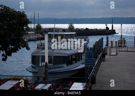 Sonnenlicht glitzert ab Neuenburger See. Der Port de Neuchâtel steht im Vordergrund; einer der Fähren ist angedockt. Frau am Pier. Stockfoto