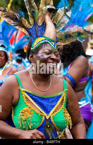 London, Notting Hill Carnival Parade, lächelnd behäbige Mitte im Alter schwarze Frau in Pfau Kostüm tanzt im Festzug Stockfoto