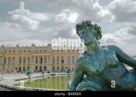 Statue und Brunnen auf dem Gelände des Schlosses von Versailles im Sommer mit dem Palast im Hintergrund. Stockfoto