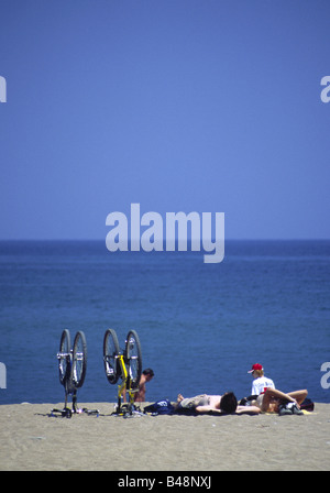 Sonnenbaden am Strand von Barceloneta liegen neben Männer umgedrehten Fahrräder, träge beobachten eines vorbeifahrenden Bootes, Barcelona, Spanien Stockfoto