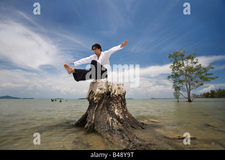 Ein Mann, balancieren auf einem Baumstumpf an einem Strand in Koh Lanta, Thailand Stockfoto