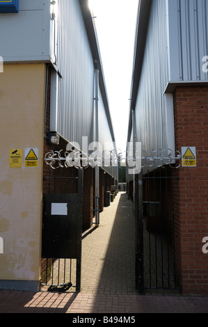 Schmale Gasse zwischen zwei Gebäuden, die durch Stacheldraht, ein Tor und CCTV, mit Warnschildern geschützt. Porträt. Stockfoto