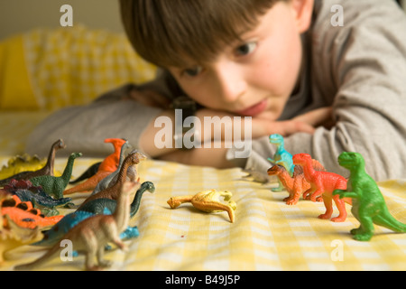 Ein pre-teen junge blickt über eine Horde von bunten Spielzeug Dinosaurier organisiert in Schlacht Reihen mit einem gefällten Diplodocus zwischen Ihnen Stockfoto