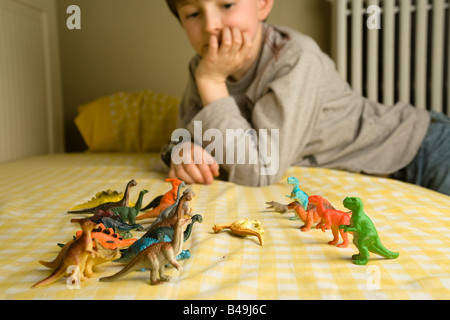 Ein pre-teen junge blickt über eine Horde von bunten Spielzeug Dinosaurier organisiert in Schlacht Reihen mit einem gefällten Diplodocus zwischen Ihnen Stockfoto