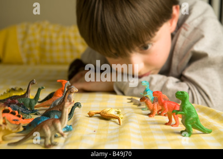 Ein pre-teen junge blickt über eine Horde von bunten Spielzeug Dinosaurier organisiert in Schlacht Reihen mit einem gefällten Diplodocus zwischen Ihnen Stockfoto