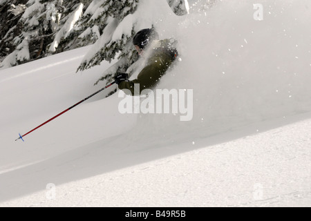 Ein Skifahrer im Tiefschnee mit einem großen Spray von Schnee über die Schulter Stockfoto