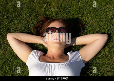 Frau auf dem Rücken, Sonnenbaden auf dem Rasen mit Sonnenbrille im freien legen. Draufsicht. Stockfoto