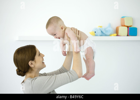 Mutter anhebende Baby in der Luft, beide Lächeln einander an Stockfoto