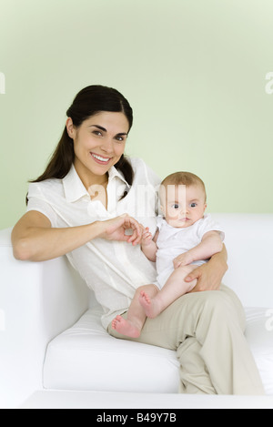 Frau halten Baby auf dem Schoß, lächelnd in die Kamera Stockfoto