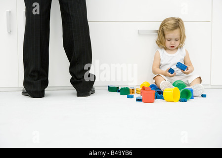 Kleinkind Mädchen sitzen auf dem Boden neben Vaters Beine, spielen mit Spielzeug Stockfoto