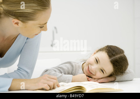 Mutter und Tochter schauen Buch zusammen, Mädchen Kopf auf Arme ruhen Stockfoto